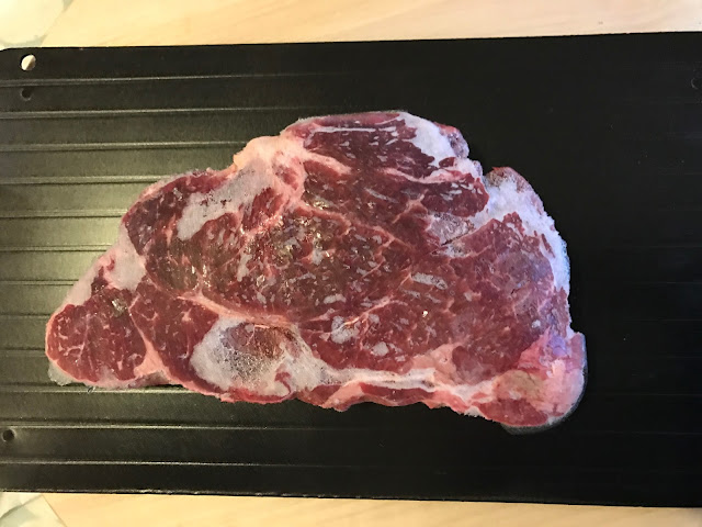 A black aluminium tray with a large frozen piece of beef steak on