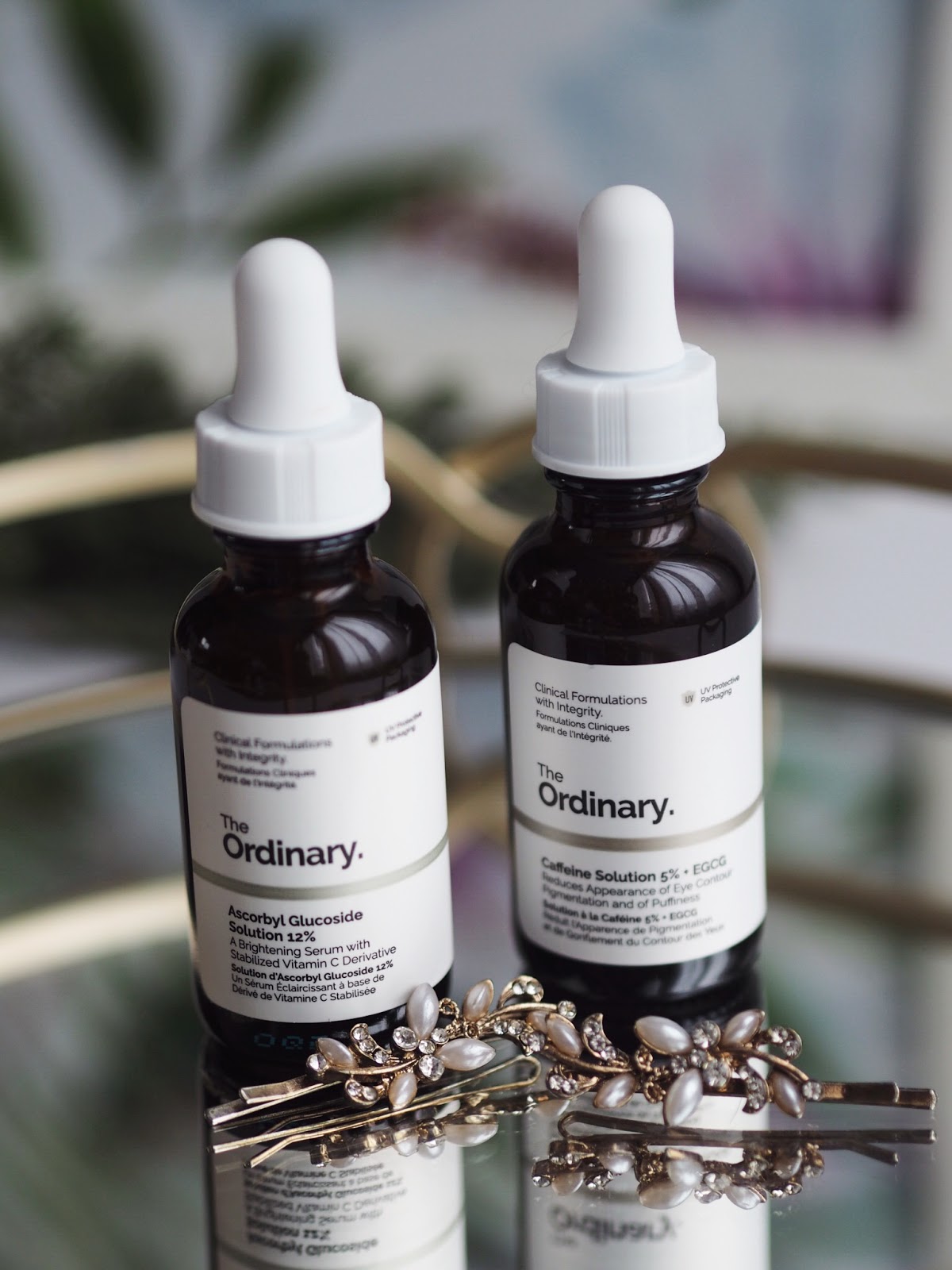Two brown, sunlight sensitive bottles of the ordinary skincare on a mirrored base with two hair clips