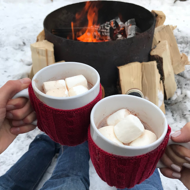 Erica Cook and Luke Boyer holding hot chocolates by a fire at Mount Engadine Lodge