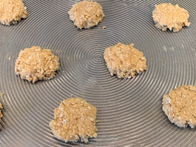 flattened spoonfuls of Coconut Oat Cookie dough on a cookie sheet