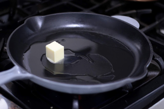 A cast iron skillet on the stove with butter and garlic in it. 