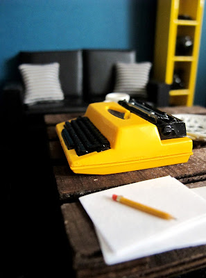 Modern one-twelfth scale miniature lounge with a typewriter sitting on a pallet coffee table.