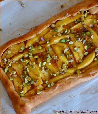 Glazed Mango Tart with Pistachios, a crescent tart topped with ripe mango slices, baked with a glaze, then topped with crunchy topped pistachios. | Recipe developed by www.BakingInATornado.com | #recipe #dessert