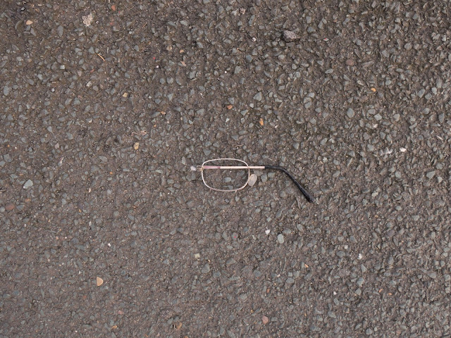 Half a pair of glasses on tarmac pavement.