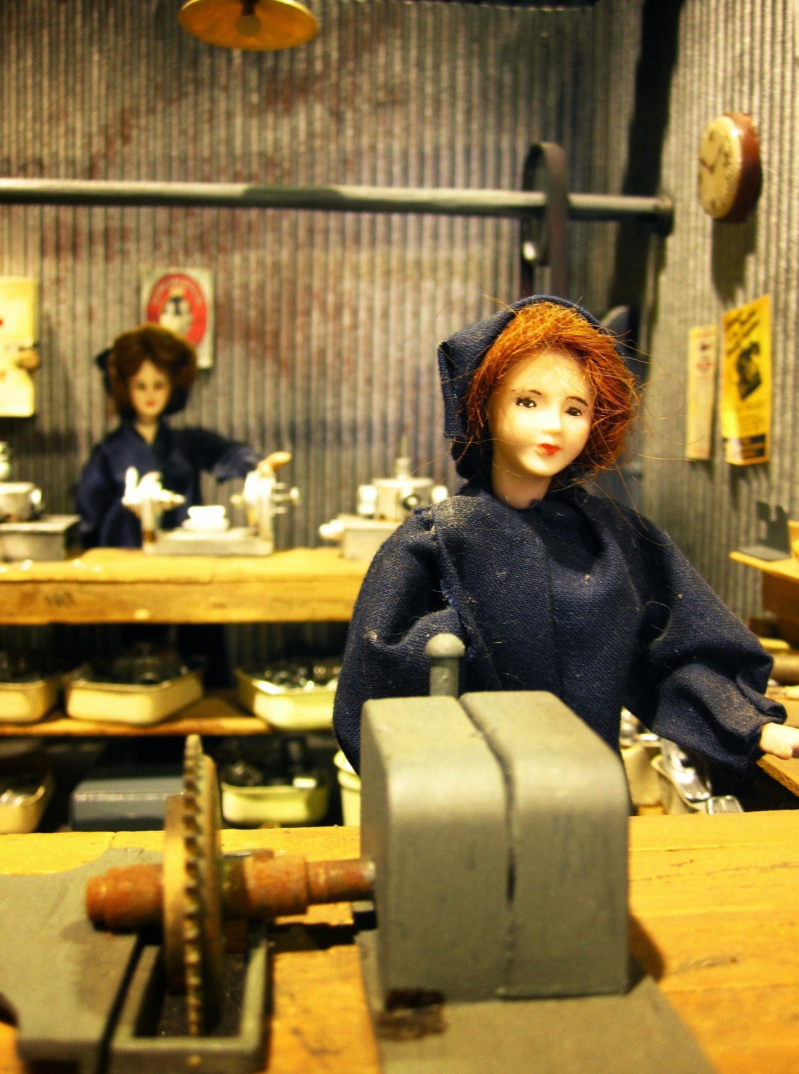 Dolls house miniature of a wartime munitions factory with two dolls at machines.
