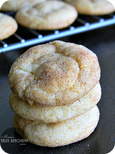 3 soft baked cookies stacked on top of each other in front of a batch of cookies cooling on a rack
