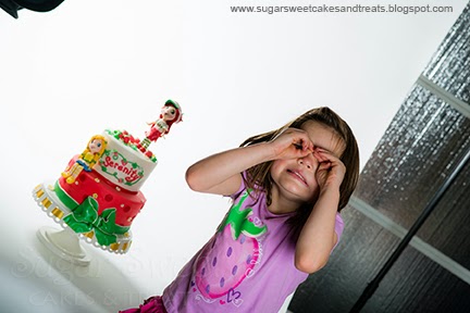 Cake being photographed professionally with birthday girl making funny faces in background.