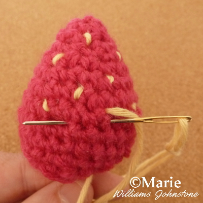 darning needle sewing yellow stitches into a amigurumi strawberry design crochet