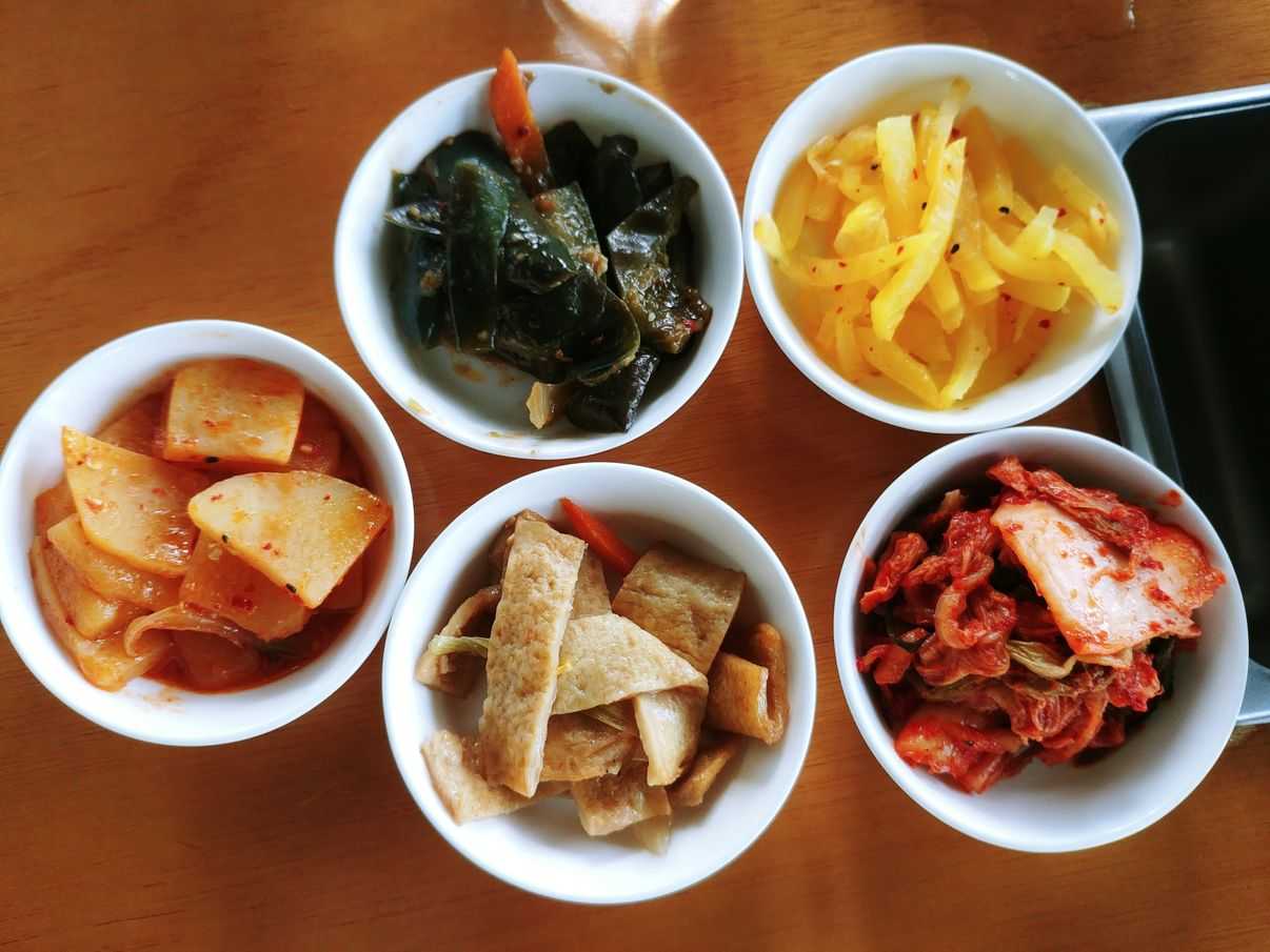 banchan or side dishes of kimchi, egg, seafood roll, potato, eggplant, and turnip at nice two Meat u