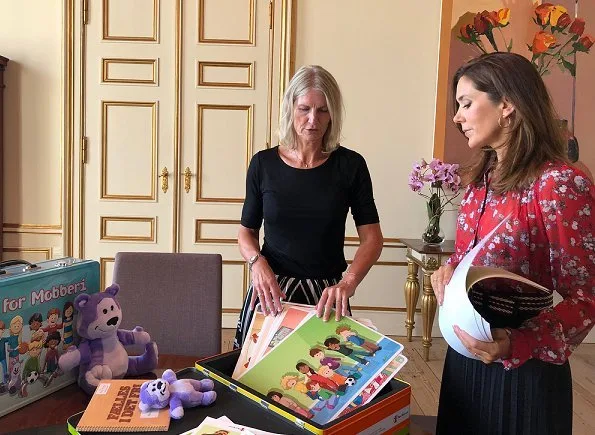 Crown Princess Mary with a dark skirt and a red flower print blouse, gold earrings during a meeting. Fri for Mobberi/Free of Bullying