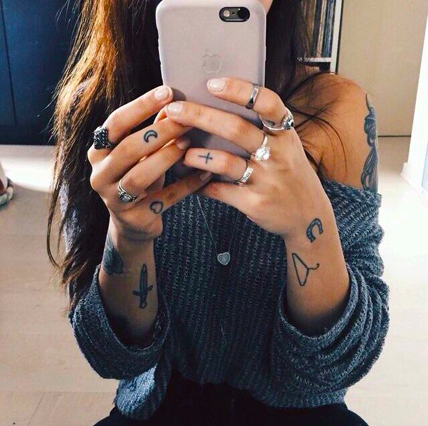 Chica sacándose una foto frente al espejo, lleva tatuajes pequeños en brazos