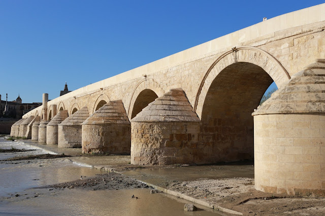 Puente romano de cerca con el río a sus pies y el cielo azul de fondo.