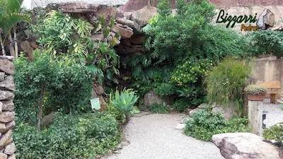 Detalhe da construção da entrada da gruta de pedra, com pedra moledo, com execução do paisagismo, com o banco de pedra e o piso de pedrisco.