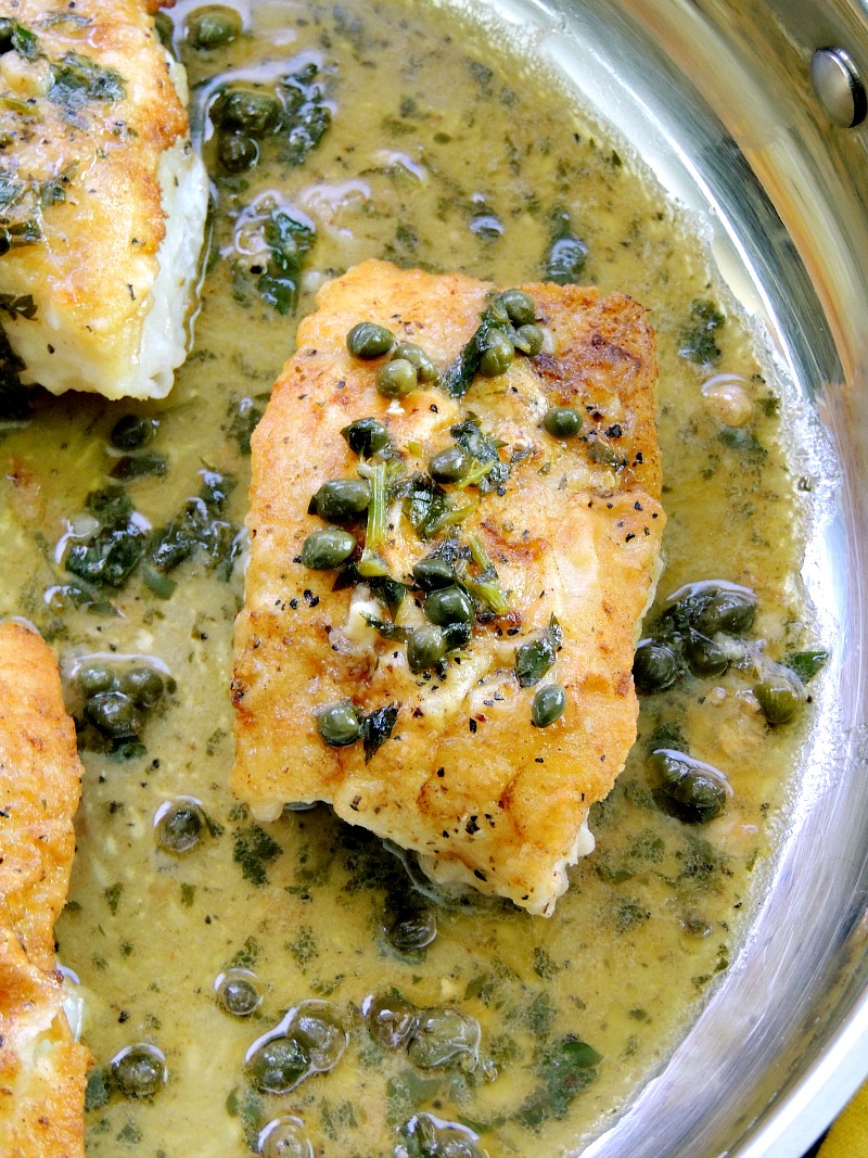 Pan-Roasted Cod with Lemon White Wine Sauce is seared on the stove, then finished in the oven for perfectly flaky fillets. Then topped with an amazing lemon white wine butter sauce. #fish #wine #butter #lemon #sauce #glutenfree #recipe | bobbiskozykitchen.com Close up of Pan-Roasted Cod with Lemon White Wine Sauce in a silver skillet.