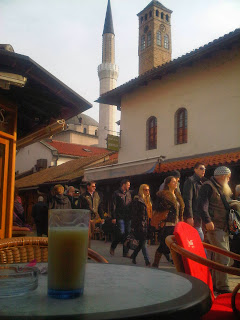Glass of boza on a table in the old town in Sarajevo with people passing by.