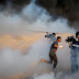 Cameramen film as a Palestinian demonstrator reacts to tear gas