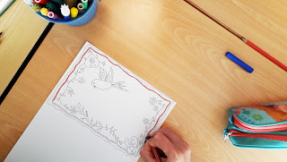 Uma mão a pintar um postal com desenhos inspirados nos lenços dos namorados portugueses