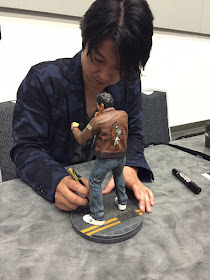Masaya Matsukaze signing a Ryo Hazuki figurine