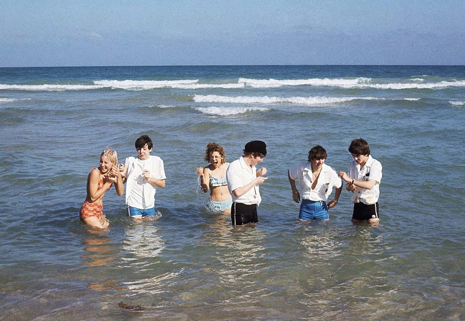 The Beatles wade in the surf in Miami, Florida in February of 1964, with unidentified women.