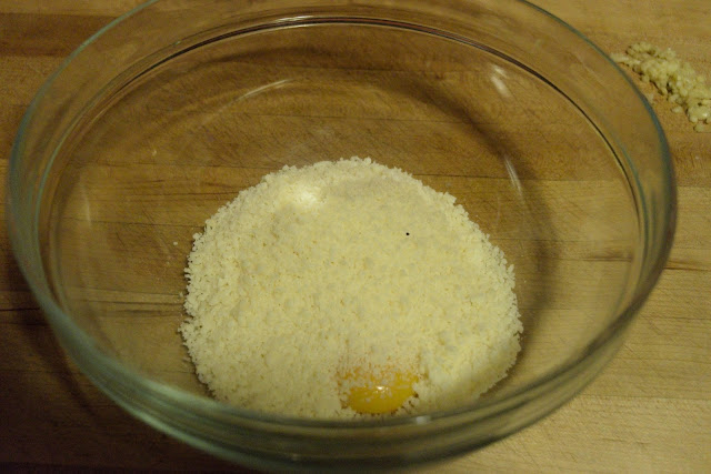 Freshly grated Parmesan cheese being added to the mixing bowl with the egg yolks.  