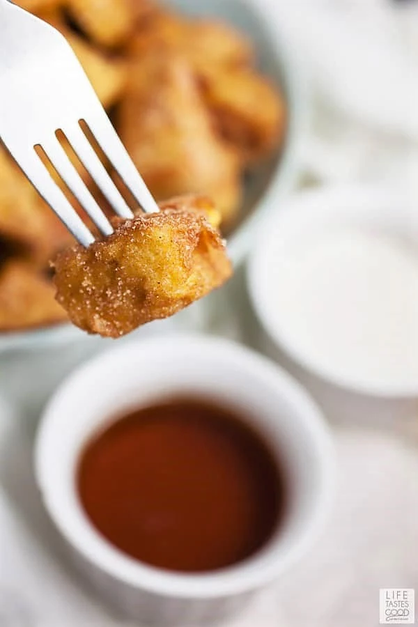A cinnamon french toast bite on a fork being dipped into cinnamon maple syrup dipping sauce