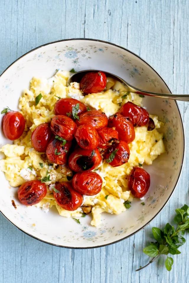 Goat Cheese Scrambled Eggs with Blistered Tomatoes is a rich and decadent breakfast dish that is made by mixing creamy goat cheese into fluffy scrambled eggs and topping them with bold garlic and herb-seasoned blistered tomatoes.