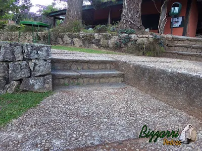 Escada de pedra folheta nesse tom de cor de pedra cinza escuro sendo uma pedra de granito apicoada. Escada de pedra com os muros de pedra e os caminhos com pedregulho do rio.