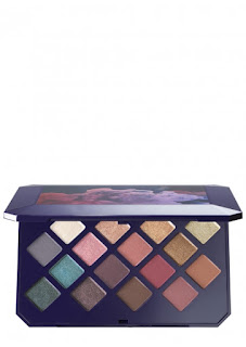 A medium sized black and blue plastic case containing a rectangular glass mirror, and diamond shaped pans containing different metallic and matte eyeshadows including blues, greens and golds on a bright background. \