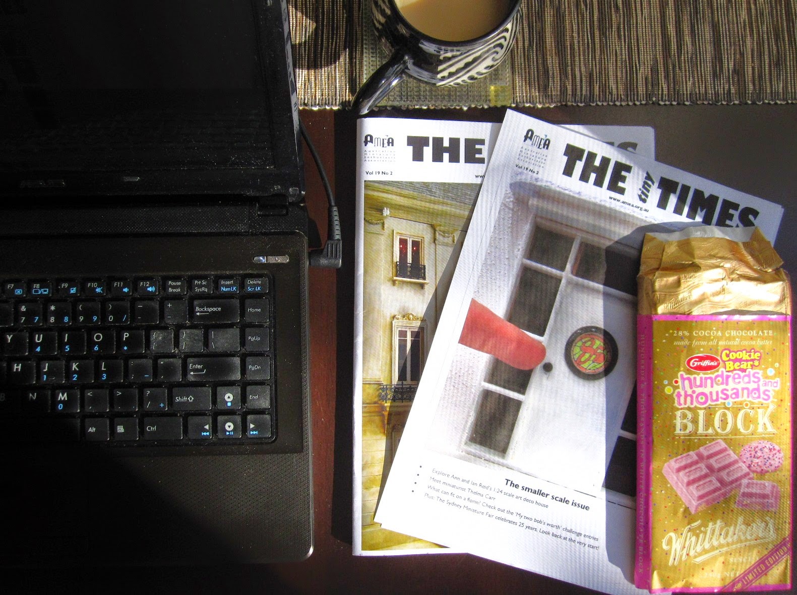 Laptop and mug of tea, with two issues of The tiny Times and a bar of Whittaker's hundreds and thousands chocolate next to it.