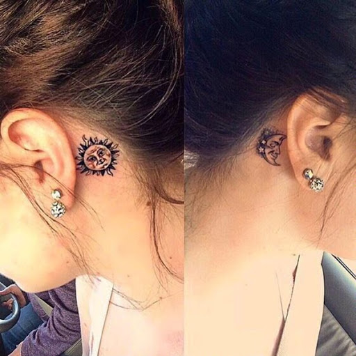 Uma personificação da lua crescente é embelezado com um trio de estrelas no preto e cinza tatuagem prestados por trás do portador da orelha direita.