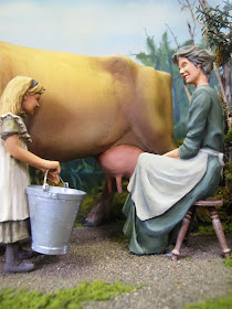 Model of a 19th-century woman milking a cow, with a child standing next to her with a bucket.
