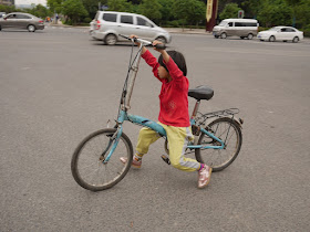 small girl walking a bike while siting on the crossbar