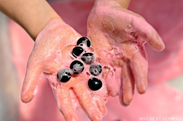 Child's hands showing pink bubbles and black seeds from a watermelon sensory activity