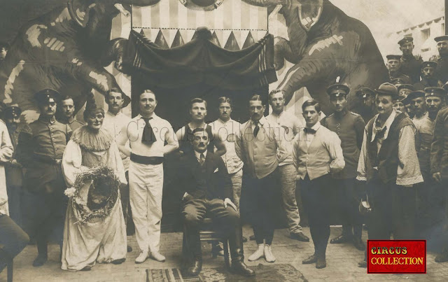 Ancienne carte postale d'une troupe de cirque posant devant la façade  du cirque