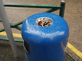 trash can with ashtray on top filled with cigarette butts and water in Macau