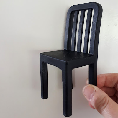 Black plastic doll's chair being held up.