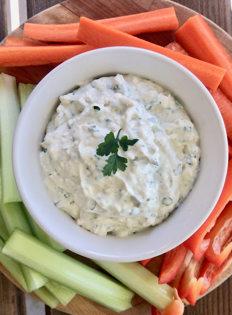 Bowl of fresh garlic and herb dip surrounded by cut fresh vegetables.