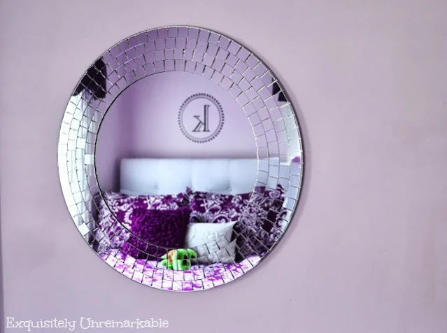 Round Mosaic Mirror on a pale purple wall reflecting purple bedding