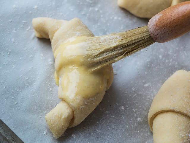 Brushing egg wash on a yeast dough crescent.