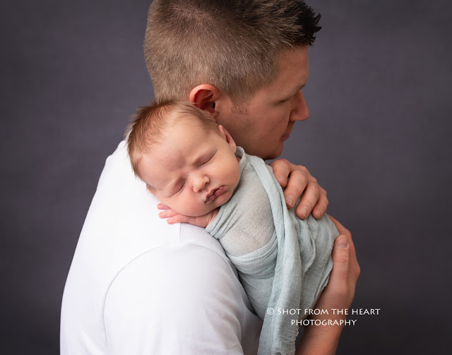 dad posing with newborn baby against gray background