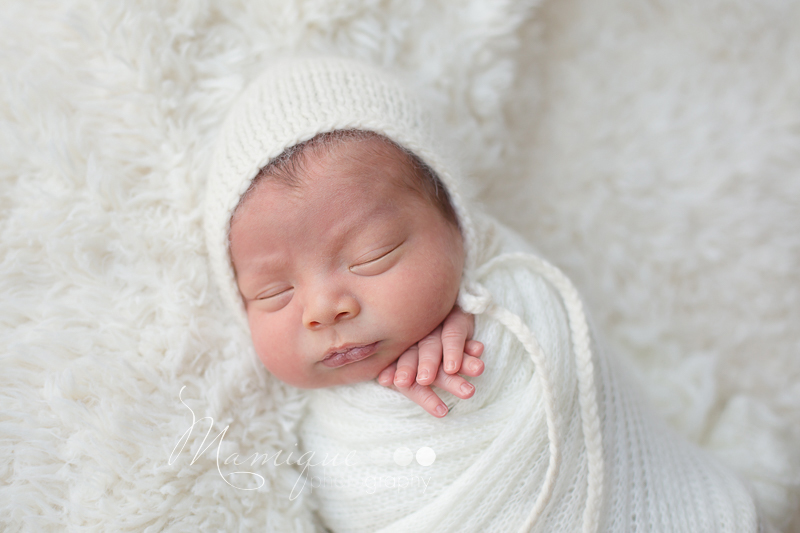 Baby infant boy sleeping wrapped in cream blanket wearing a hat