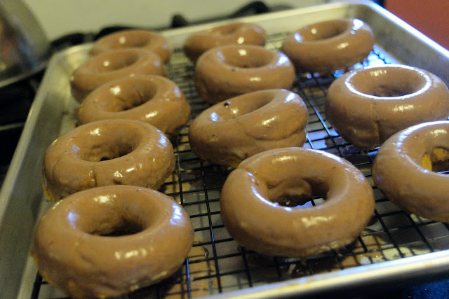 The glazed donuts, on a cooling rack and baking sheet, setting up. 