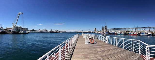 A wooden pier lined by a white railing leading into the harbour.