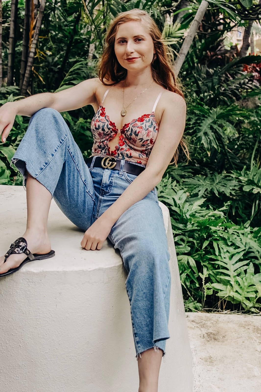 amanda burrows sits in oahu, hawaii. she is wearing a floral bodysuit from forever 21 and a pair of hi-rise wide-leg jeans from target. she also has one a gucci belt from amazon. 