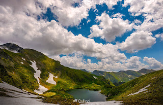  clear lake in mountains with snow and grass on rocky hillside. dramatic weather in picturesque summer scenery