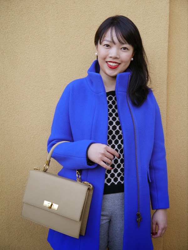 Cobalt blue cocoon coat worn with graphic black-and-white sweater, grey ankle trousers, burgundy pony hair smoking slippers, and a structured top-handle bag.