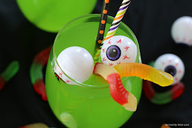 Clear glass with green punch on black background with eyeballs and gummy worms