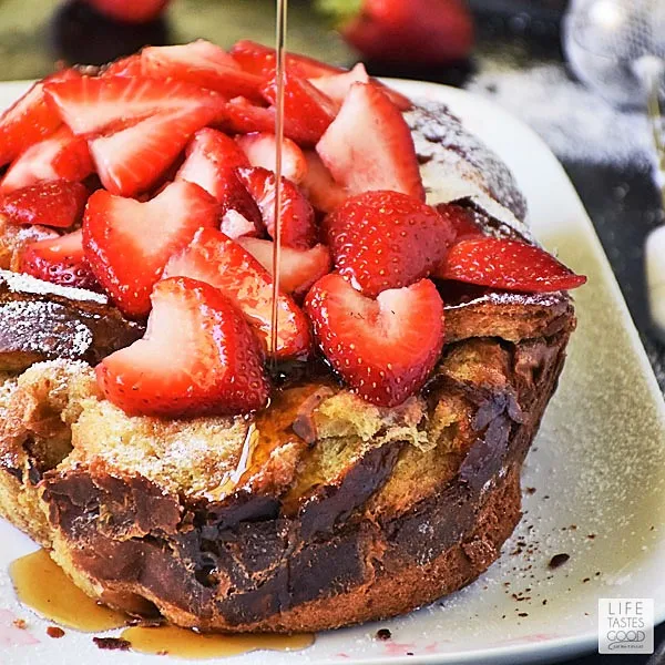 Slow Cooker French Toast topped with strawberries with maple syrup being drizzled on top