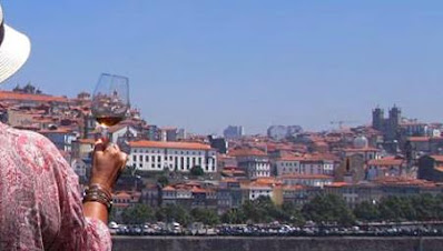 Mulher com chapéu segurando um copo de vinho do Port em frente à cidade do Porto