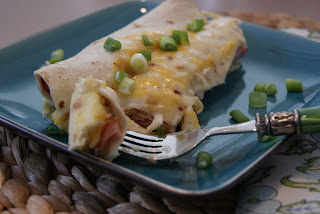 Two breakfast enchiladas topped with chives served on a blue plate ready to be eaten.